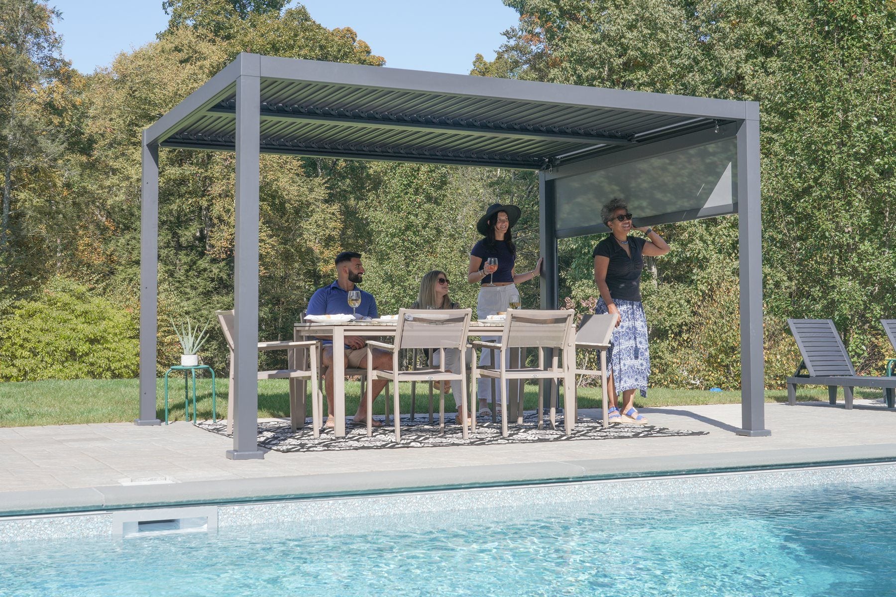 Sojag Hilo louvered aluminum pergola over a patio dining table beside a pool, a privacy panel lowered on one side