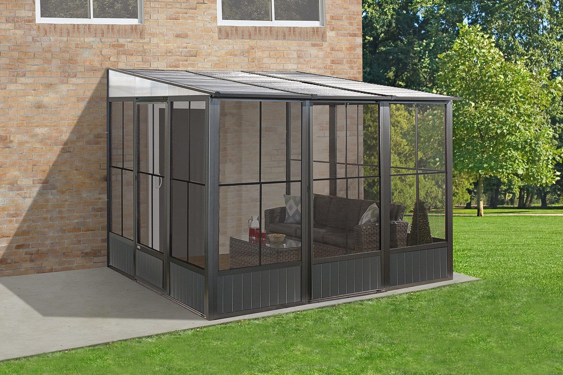 Solarium mural Sojag Korado avec fenêtres coulissantes en PVC et moustiquaires, adossé à une maison de brique