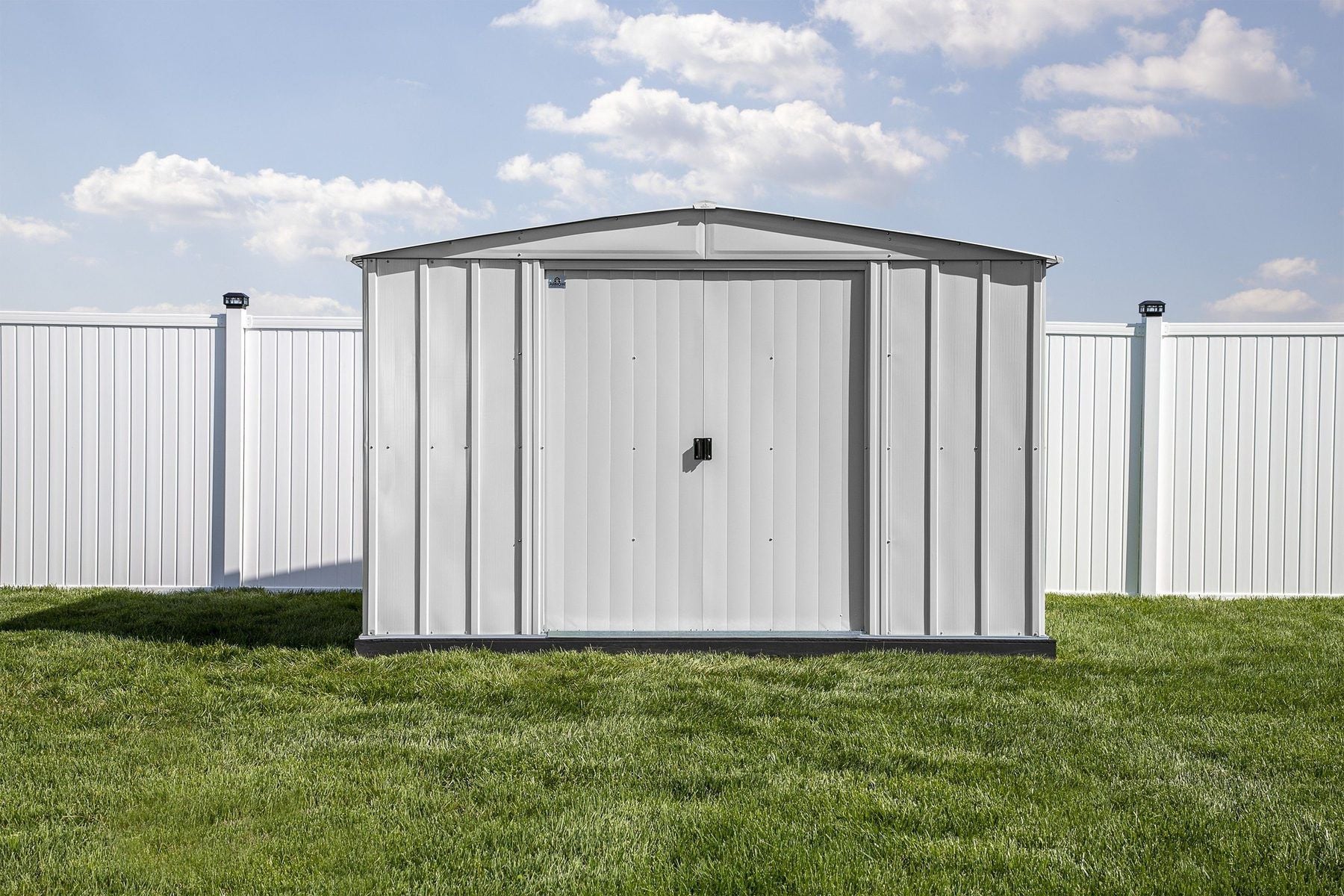 Cabanon en acier Arrow Classic gris posé bien d'équerre sur une base construite, dans une cour clôturée