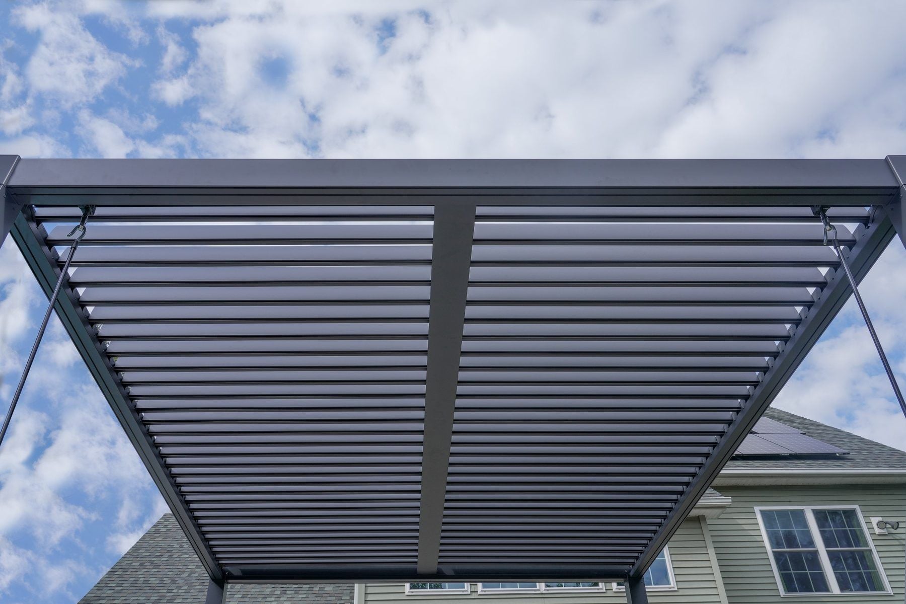 Underside of an aluminum louvered pergola roof with the blades half open against a blue sky